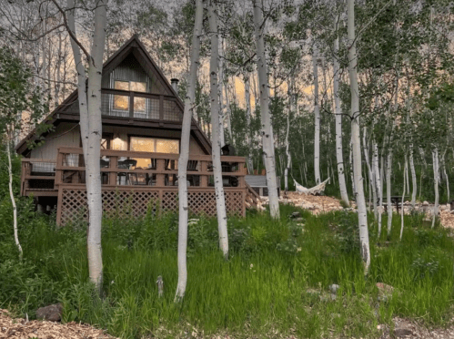 A cozy cabin nestled among tall aspen trees, surrounded by lush green grass and a serene evening sky.